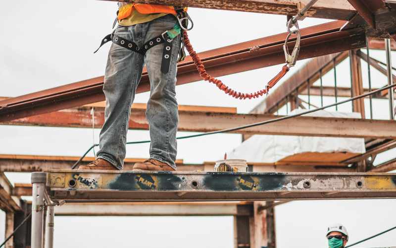 A contractor on scaffolding working on an exterior wall, holding a wooden board