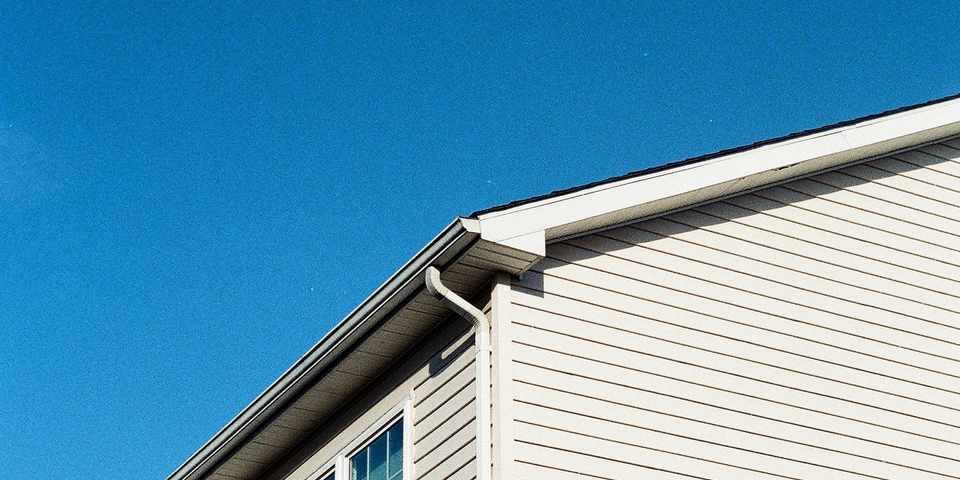 Close-up of a home's lap siding, gutter, and roofline against a clear blue sky
