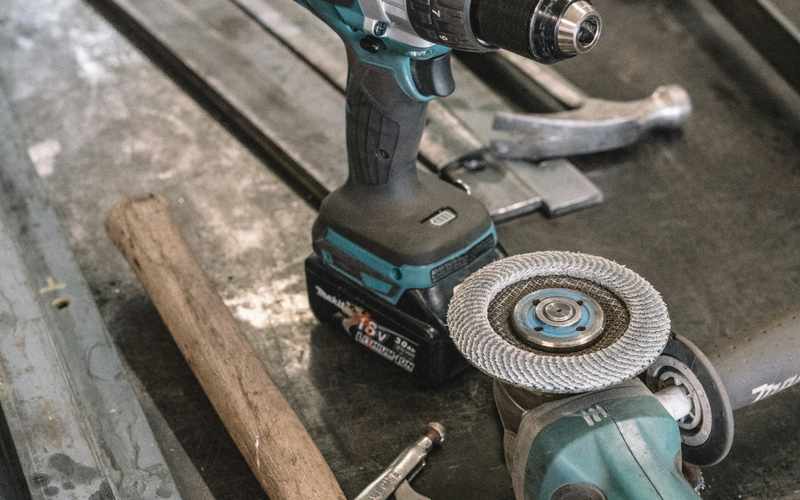 A cordless drill and angle grinder laid out on a jobsite floor