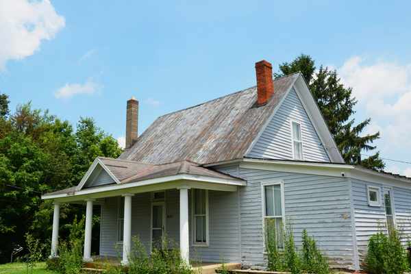 An older home exterior with a weathered metal roof and light-colored wood siding