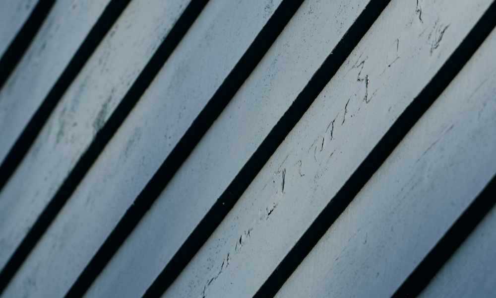 Close-up of diagonal weathered painted board siding with dark shadow gaps between planks
