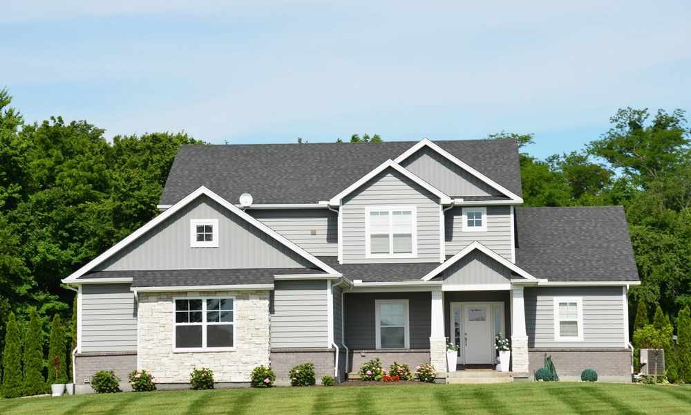 Two-story home exterior with gray vinyl siding, white trim, and stone accents