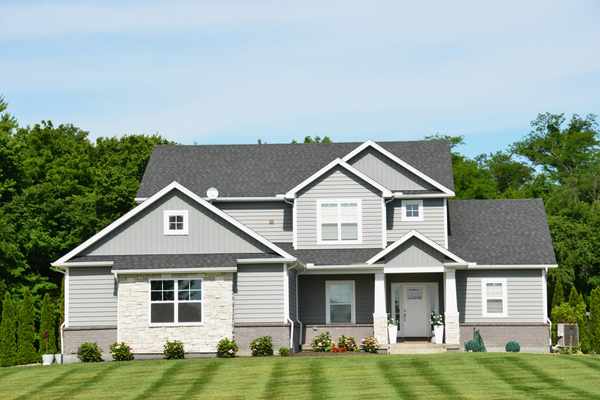 Two-story home exterior with gray vinyl siding, white trim, and stone accents